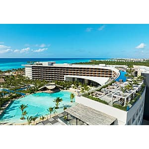 Tropical all-inclusive resort poolside with guests enjoying amenities surrounded by palm trees and ocean views.