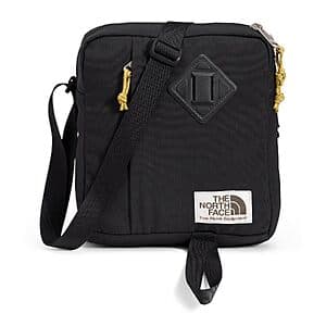 The North Face Berkeley Crossbody Bag in black with mineral gold accents, featuring a compact rectangular design with an adjustable crossbody strap.