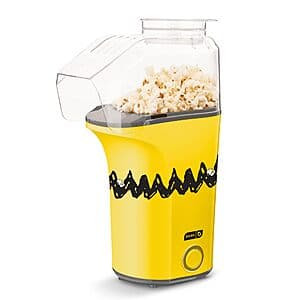 White Peanuts DASH brand air popcorn maker with removable top chute and measuring cup, sitting on countertop.